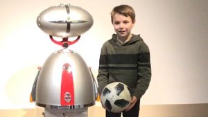 Ein Junge steht neben einem Roboter und hält einen Fußball in den Händen.