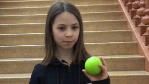 Ein Mädchen mit hellbraunen Haaren hält einen Hockeyball in die Kamera.